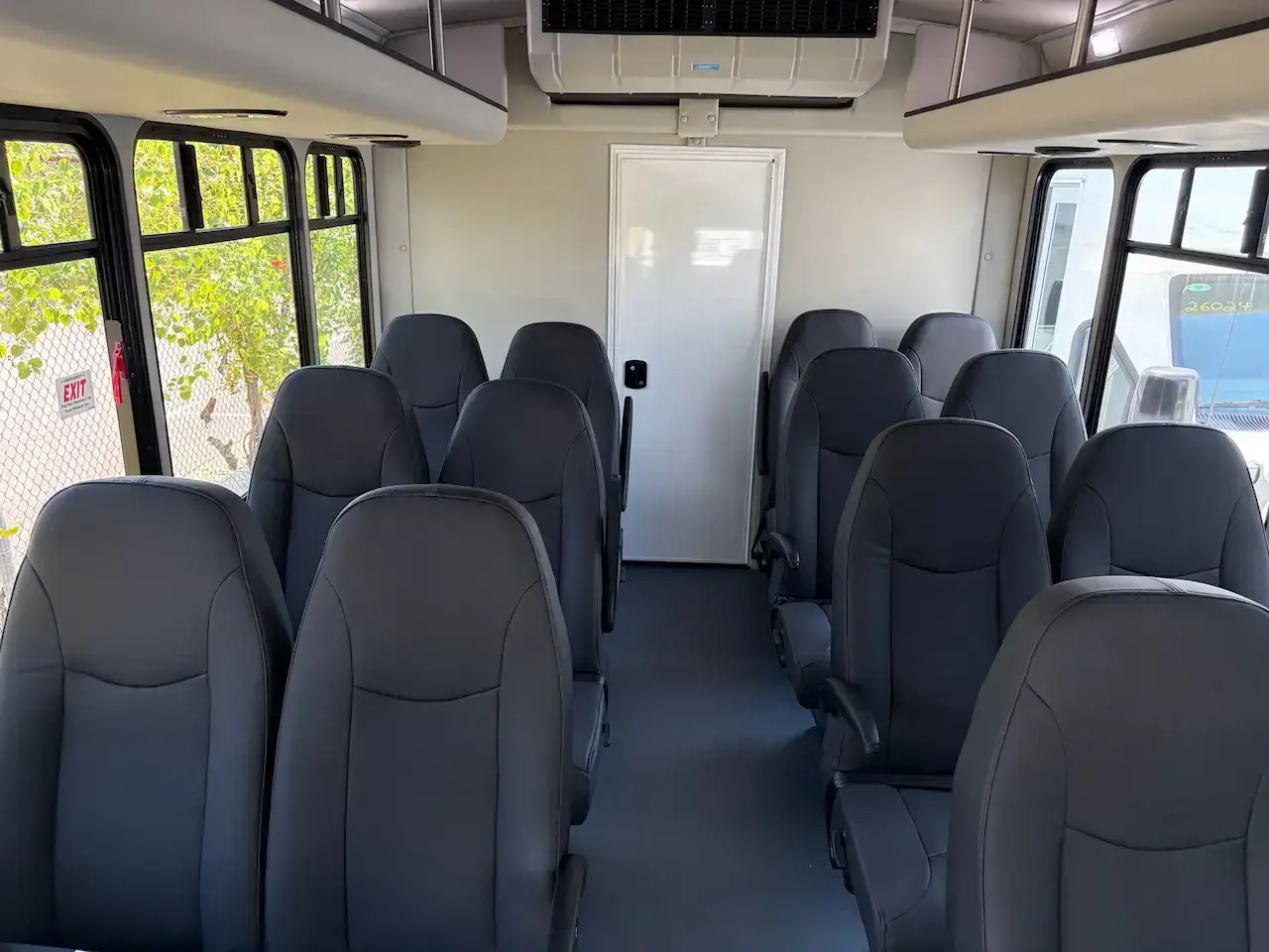 Interior of a 15 passenger Starcraft Allstar bus with high back recliner seats, arm rests at the aisle, a full length center aisle, overhead luggage racks, and a rear luggage wall
